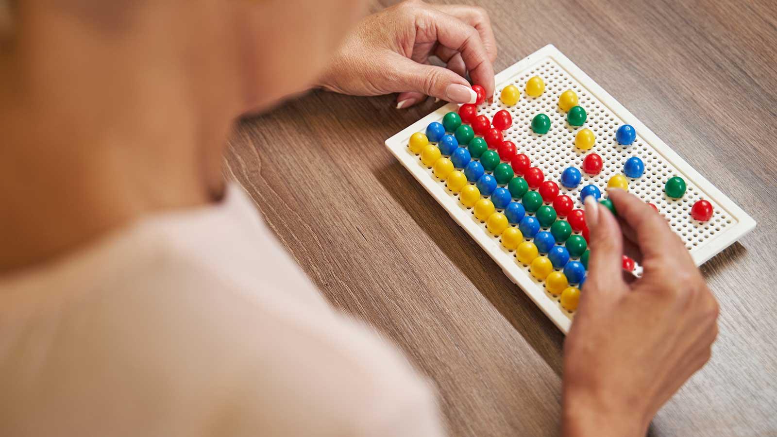 一位女士在esball国际平台客户端的一个代表职业治疗项目的板子上摆放彩色的钉子 